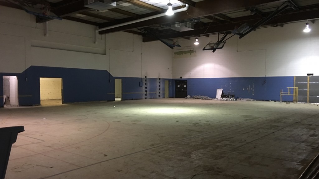 In the gym, basketball backboards remain, but bleachers and the worn plastic floor have been removed. One of the major elements of the renovation will occur behind the blue paint at left, where a larger fitness room will be installed.